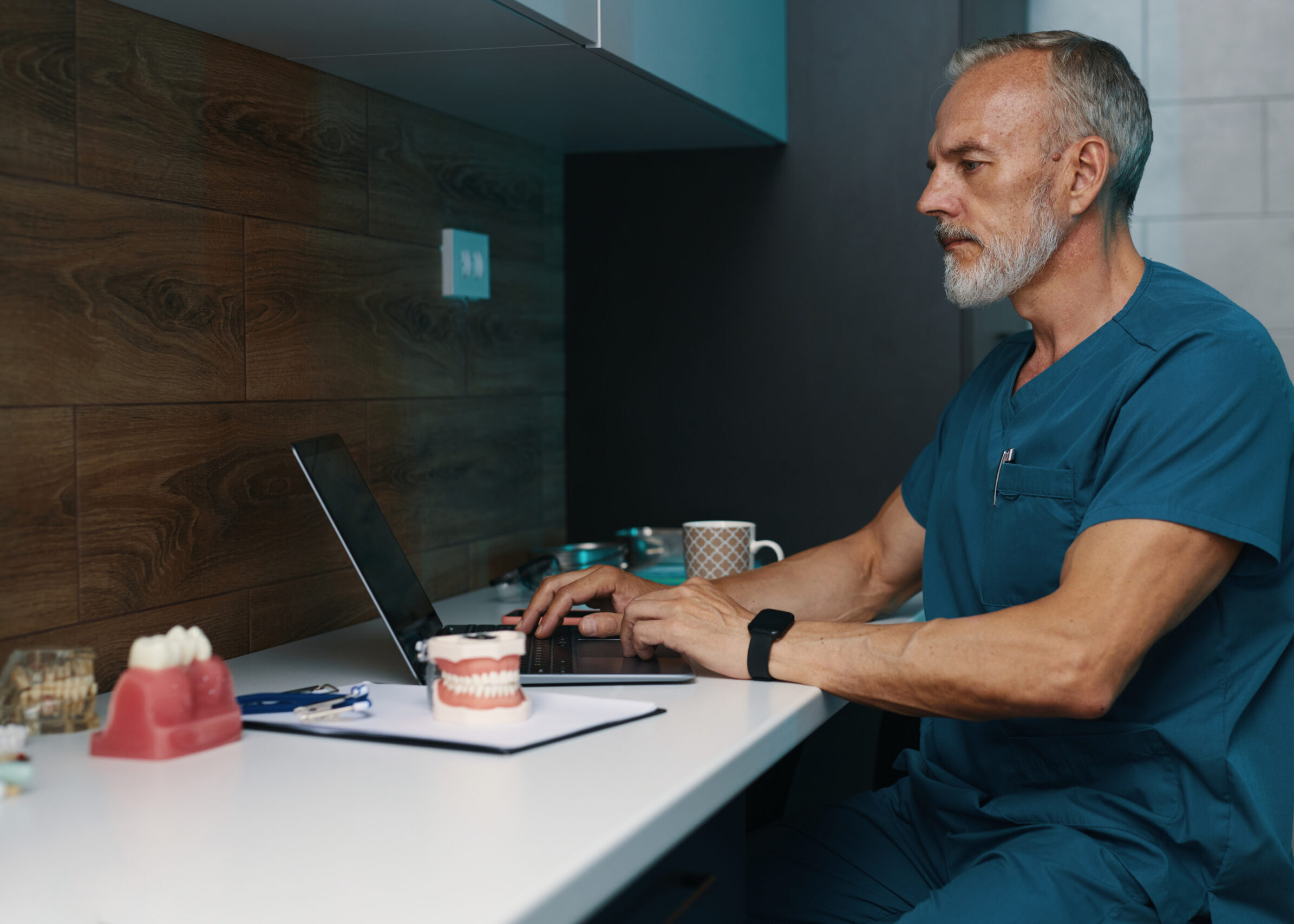 Working Senior Doctor in Blue Scrubs Using Laptop